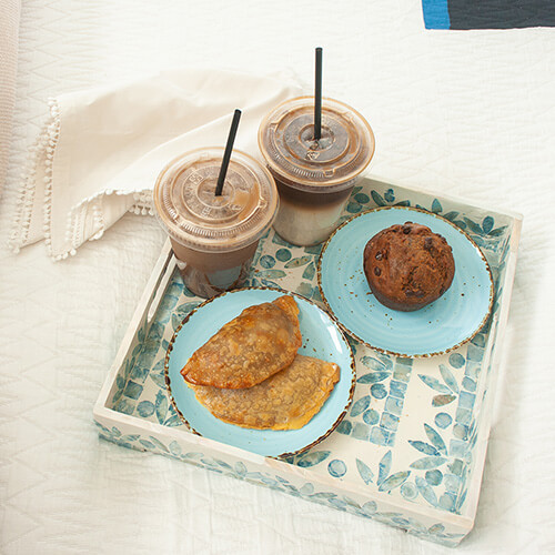 Empanadas, muffin and coffee drinks sit on a bed tray